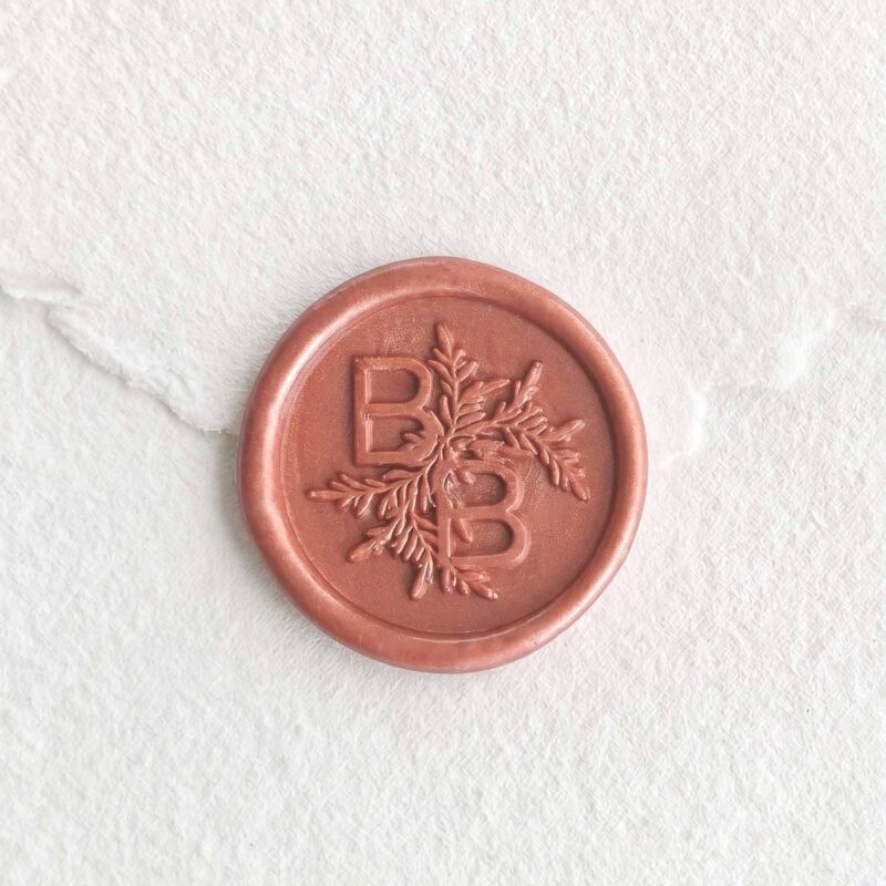 Sello de lacre Oro Rosa con iniciales sobre papel artesanal blanco