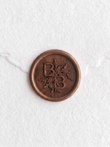 Sello de lacre Bronce con iniciales sobre papel artesanal blanco