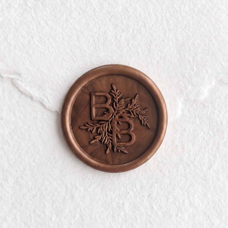 Sello de lacre Bronce con iniciales sobre papel artesanal blanco