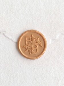 Sello de lacre Oro Champagne con iniciales sobre papel artesanal blanco