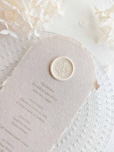 Sello de lacre adhesivo con diseño de flores vintage de estilo clásico colocado sobre un menú de boda de papel artesanal.