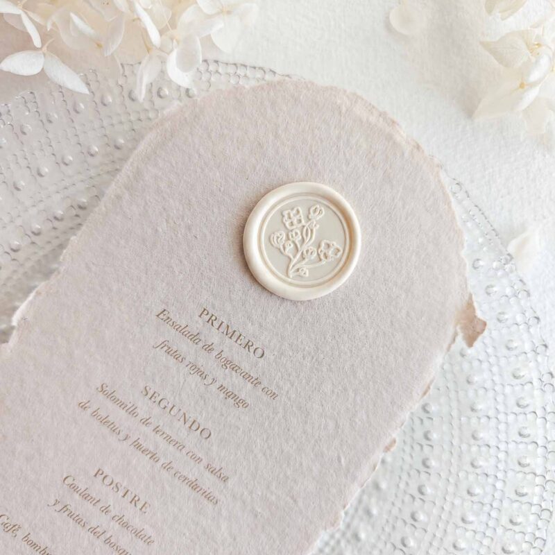 Sello de lacre adhesivo con diseño de flores vintage de estilo clásico colocado sobre un menú de boda de papel artesanal.