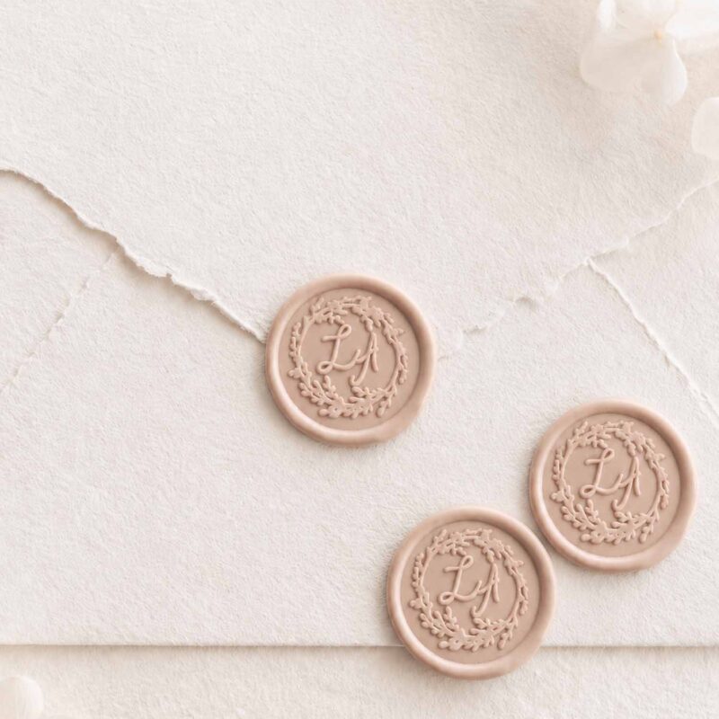 Sello de lacre adhesivo personalizado Adaline con iniciales dentro de una guirnalda clásica sobre sobre artesanal para invitaciones de boda.