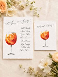 Detalle de número de mesa A6 y tarjeta de seating plan A5 Aperol Spritz en papel artesanal con ilustración de cóctel en acuarela
