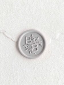 Sello de lacre Gris Niebla con iniciales sobre papel artesanal blanco