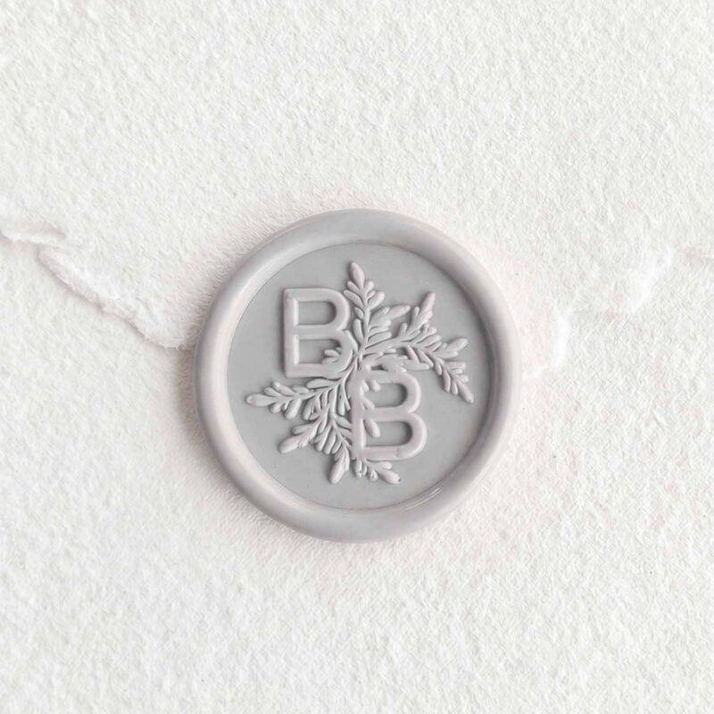 Sello de lacre Gris Niebla con iniciales sobre papel artesanal blanco
