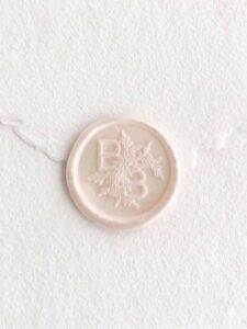 Sello de lacre Magnolia Perlado con iniciales sobre papel artesanal blanco