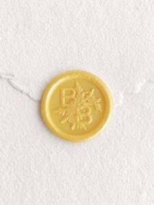 Sello de lacre Amarillo Perlado con iniciales sobre papel artesanal blanco