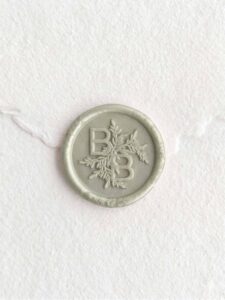 Sello de lacre Verde Perla con iniciales sobre papel artesanal blanco