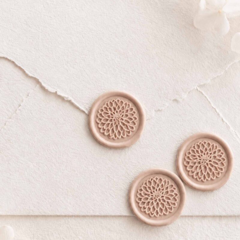 Sello de lacre adhesivo con diseño de flor dalia en relieve sobre sobre artesanal para invitaciones de boda elegantes y románticas.