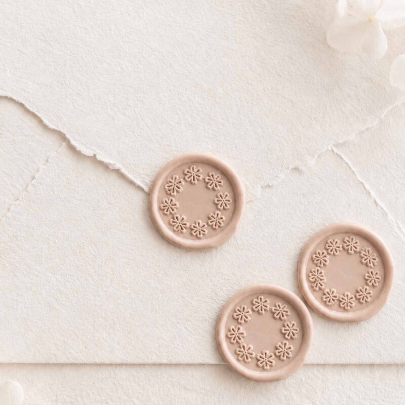 Sello de lacre adhesivo con diseño de guirnalda de flores en relieve sobre sobre artesanal para invitaciones de boda románticas y elegantes.