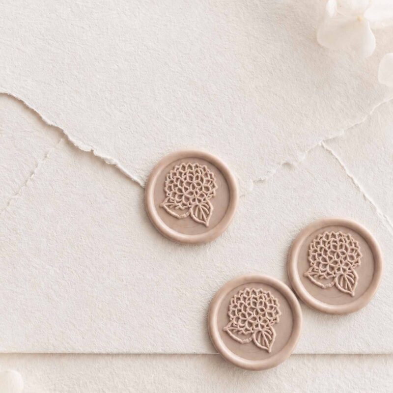 Sello de lacre adhesivo con diseño de hortensia en relieve sobre sobre artesanal para invitaciones de boda románticas y elegantes.