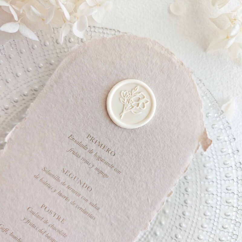 Sello de lacre adhesivo con diseño de ramo de flores colocado sobre un menú de boda de papel artesanal.