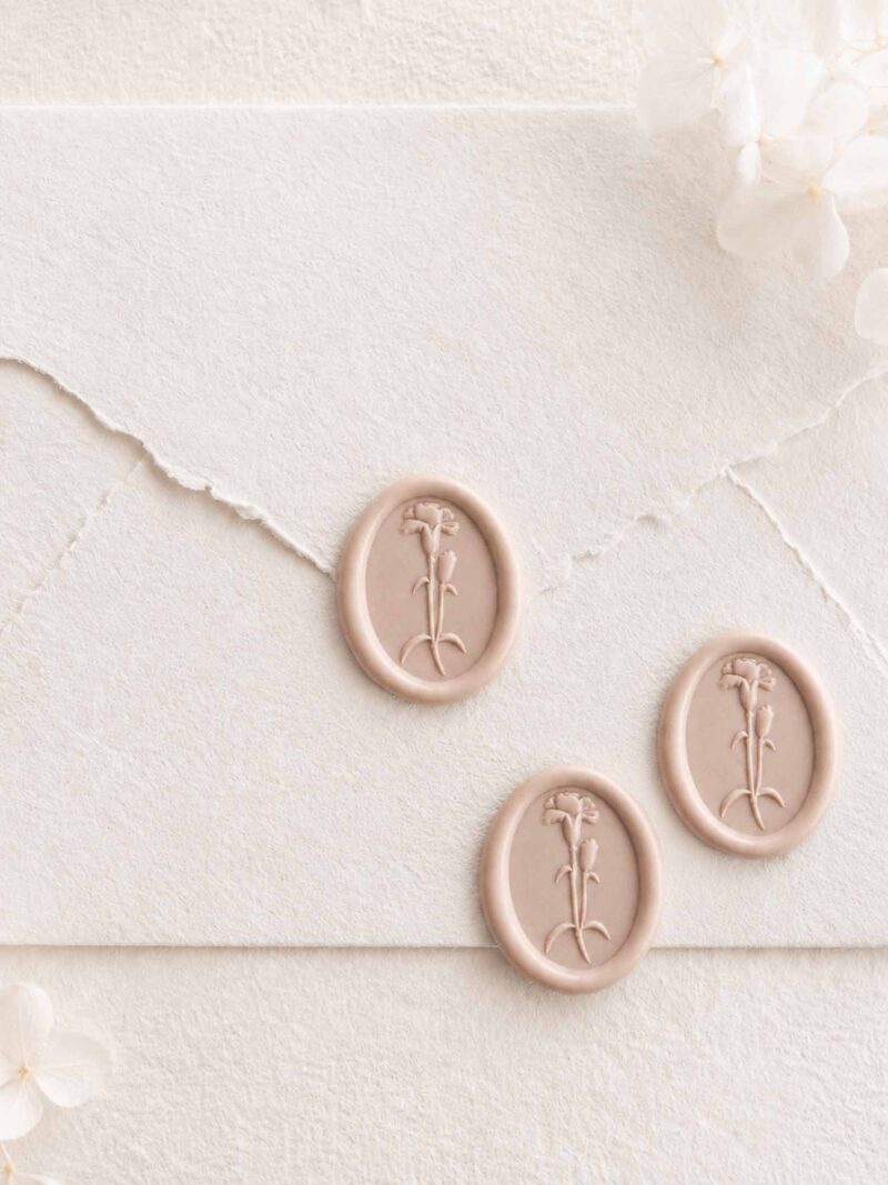 Sello de lacre adhesivo ovalado con diseño de clavel en 3D sobre sobre artesanal para invitaciones de boda románticas y elegantes.