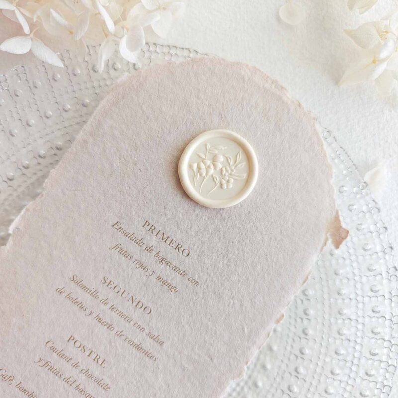 Sello de lacre adhesivo con diseño de flores en 3D colocado sobre un menú de boda de papel artesanal.