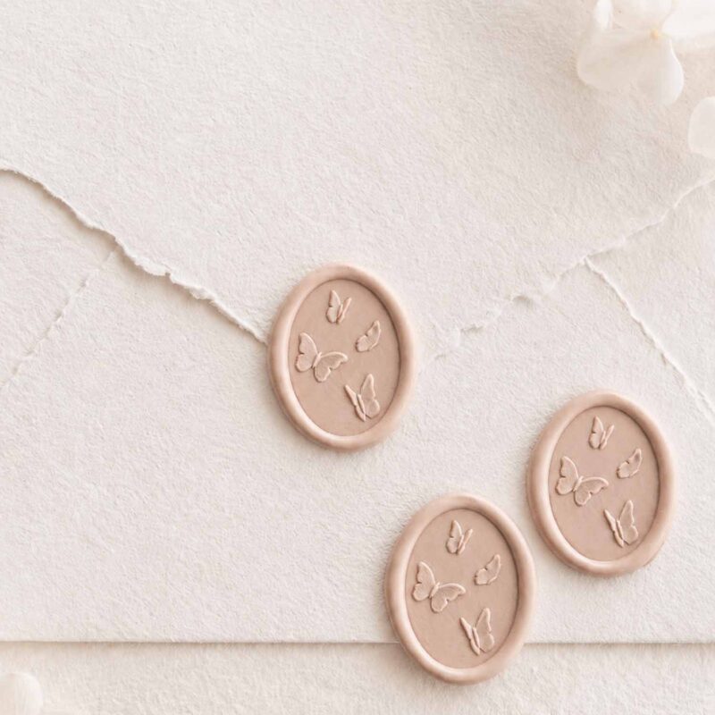 Sello de lacre adhesivo con diseño de mariposas en 3D sobre sobre artesanal para invitaciones de boda románticas y elegantes.