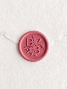 Sello de lacre Carmín con iniciales sobre papel artesanal blanco