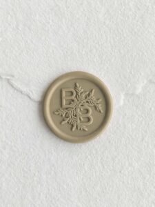 Sello de lacre Oliva con iniciales sobre papel artesanal blanco