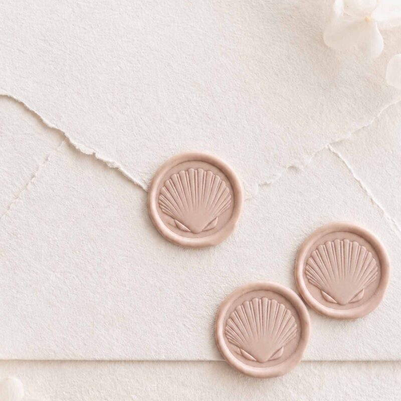 Sello de lacre adhesivo con diseño de concha en 3D sobre sobre artesanal para invitaciones de boda mediterráneas y elegantes.