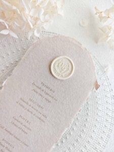 Sigillo in ceralacca adesivo personalizzato in stile classico con iniziali all’interno di una ghirlanda, applicato su un menù di matrimonio. Ideale per mantenere un’immagine coordinata in tutta la stationery dell’evento.