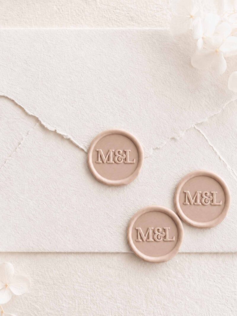 Sello de lacre adhesivo personalizado de estilo minimalista con iniciales sobre sobre artesanal para invitaciones de boda elegantes.
