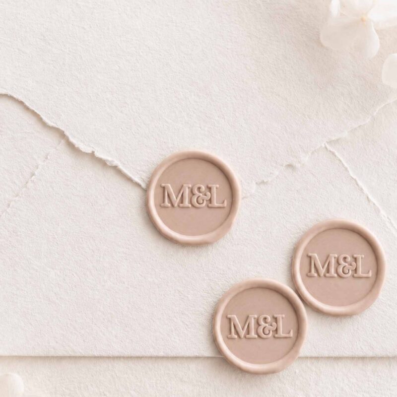 Sello de lacre adhesivo personalizado de estilo minimalista con iniciales sobre sobre artesanal para invitaciones de boda elegantes.