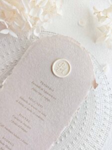 Sello de lacre adhesivo personalizado con letras caligráficas colocado sobre menú de boda artesanal.