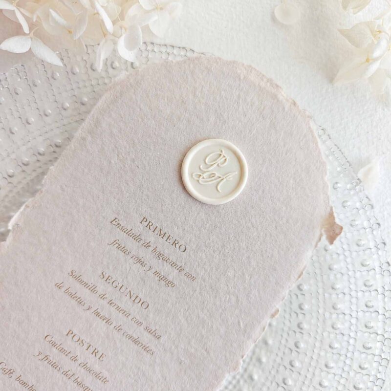 Sello de lacre adhesivo personalizado con letras caligráficas colocado sobre menú de boda artesanal.