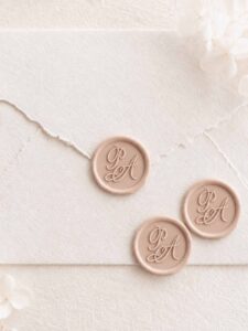 Sello de lacre adhesivo personalizado con letras caligráficas sobre sobre artesanal para invitaciones de boda elegantes.
