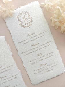 Menú de boda artesanal Adriana con monograma personalizado e impresión beige sobre papel marfil.