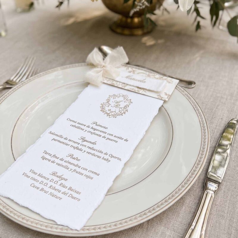 Menú de boda Adriana en papel artesanal marfil con puesto de mesa personalizado y cinta de seda marfil.