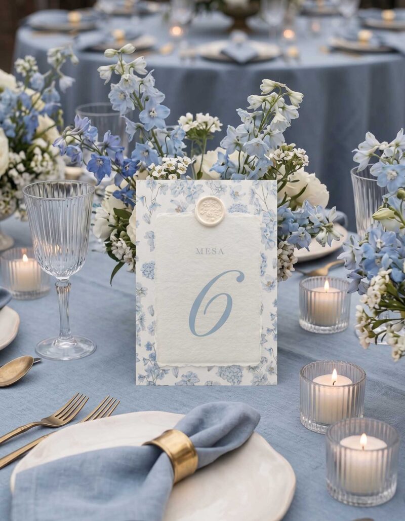 Número de mesa de boda Chloé sobre mesa azul con flores, velas y papel artesanal marfil.