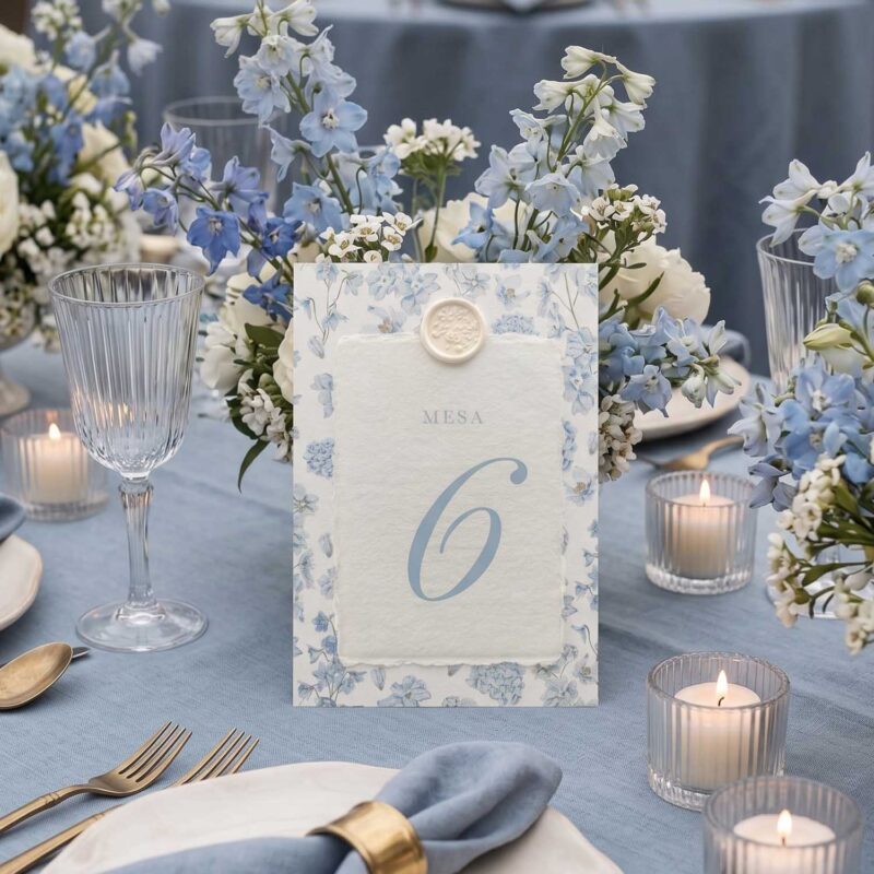 Número de mesa de boda Chloé sobre mesa azul con flores, velas y papel artesanal marfil.