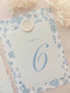 Número de mesa Chloé con papel artesanal marfil, lacre botánico y fondo floral azul empolvado.