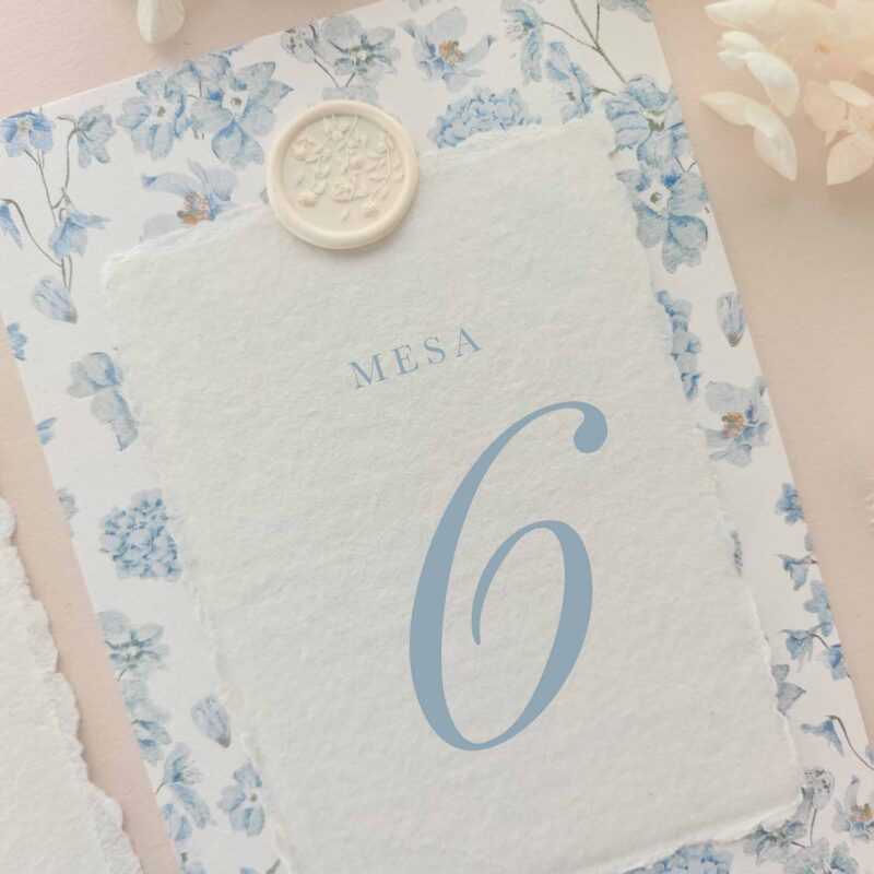 Número de mesa Chloé con papel artesanal marfil, lacre botánico y fondo floral azul empolvado.