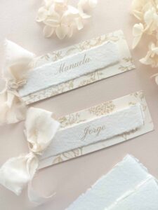 Puesto de mesa Adriana con nombre del invitado en papel artesanal, estampado floral beige y cinta de seda marfil.