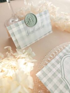 Puesto de mesa Marietta con papel vellum, nombre del invitado y sello de lacre verde.
