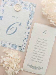 Seating plan y número de mesa Chloé en papel artesanal marfil con estampado floral azul y lacre.