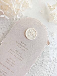 Sigillo in ceralacca adesivo con iris 3D in color avorio per decorare un menù di matrimonio in carta artigianale.
